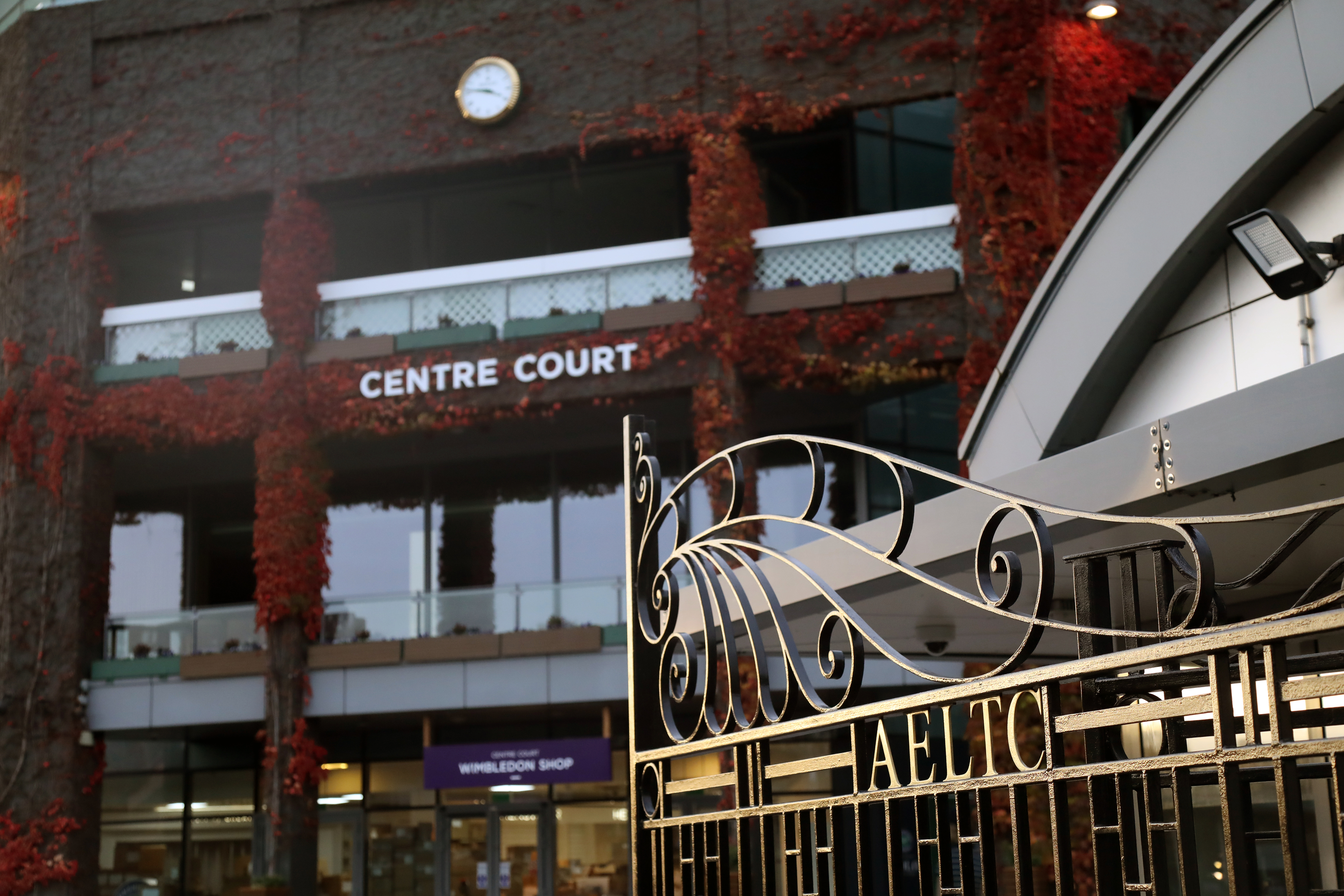Gate outside Centre Court at the All England Lawn Tennis Club in Wimbledon, with autumn leaves across the building behind.